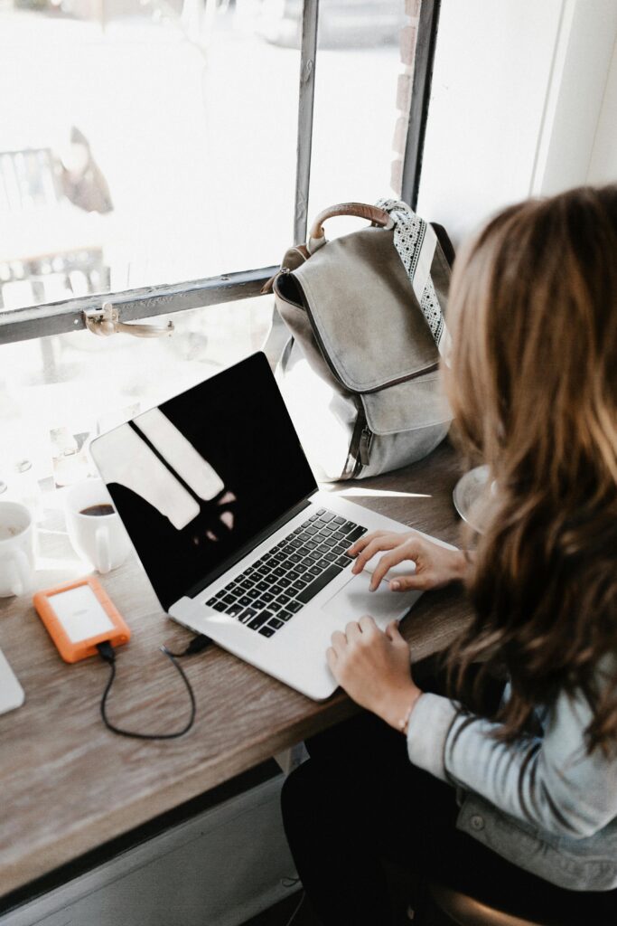 pexels-photo-3178818-3178818 A young woman works remotely at a café, using her laptop and external hard drive.